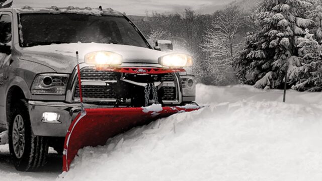 Truck with plow plowing a pile of snow with bright headlights